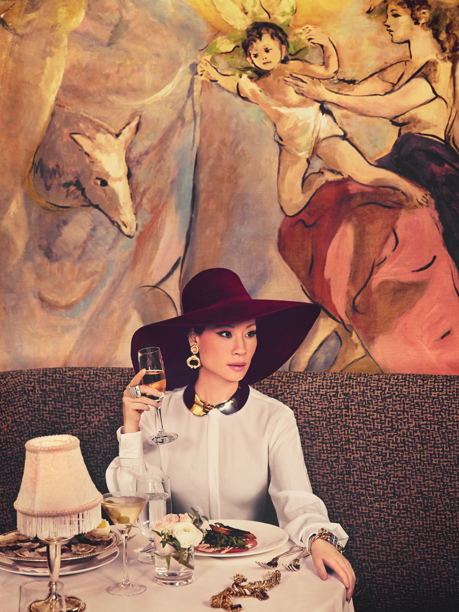 Lucy Liu of Elementary in red floppy hat drinking champagne