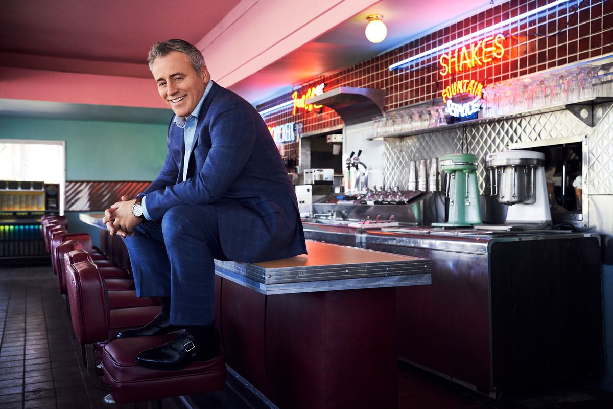 Matt LeBlanc in a vintage diner sitting on the counter with his feet on the seat.