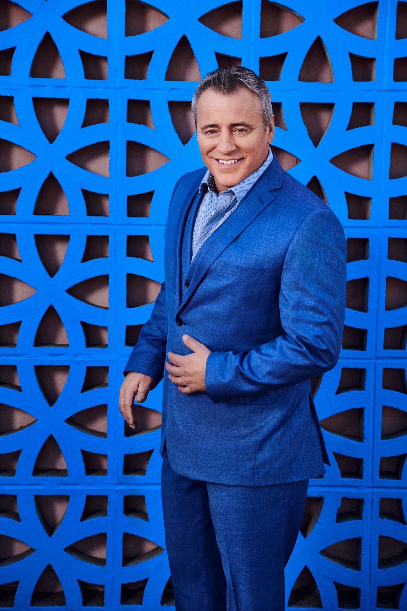 Actor Matt LeBlanc standing in front of a bright blue ornate deco wall wearing a blue suit .