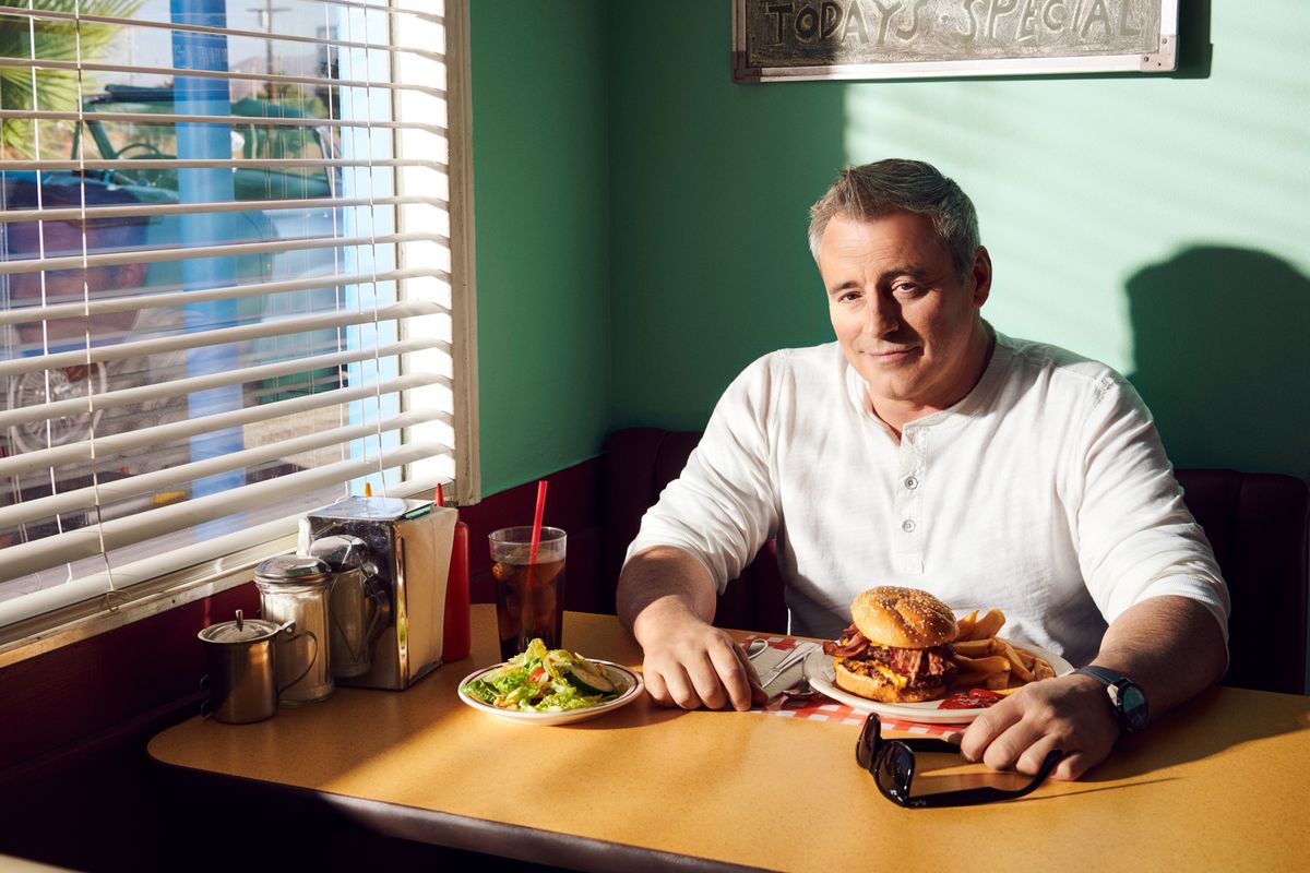 Matt LeBlanc sitting in a booth at a vintage diner with a burner and fries.