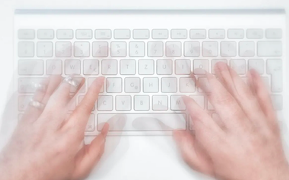 Hands typing on a white laptop