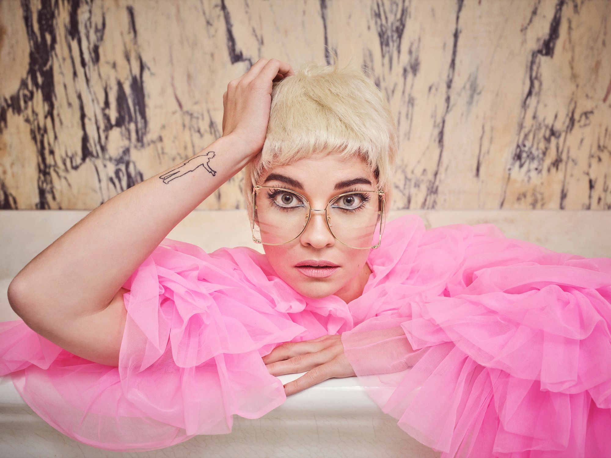 Annie Murphy wearing a short cropped blonde wig and large glasses.