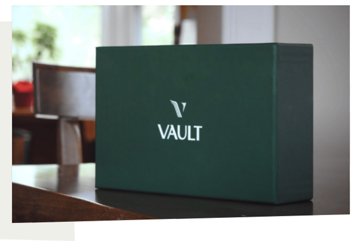 A forest green box that says Vault sits on a wood desk