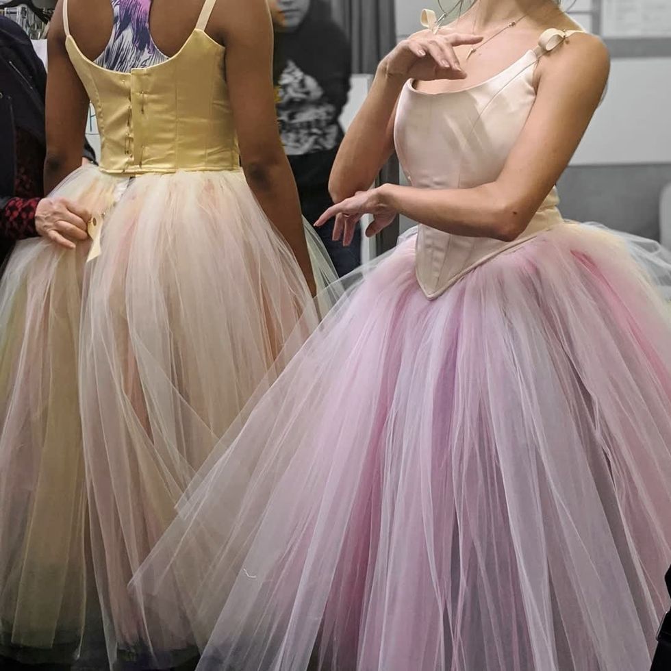 The torsos of two dancers, one in a yellow tutu and one in light pink, which still have pins in the back.