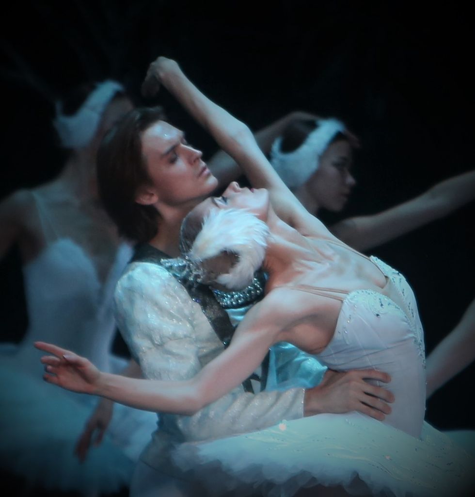 Kolesnikova, dressed in a white Odette costume leans back against Rodkin with her arms in the air.