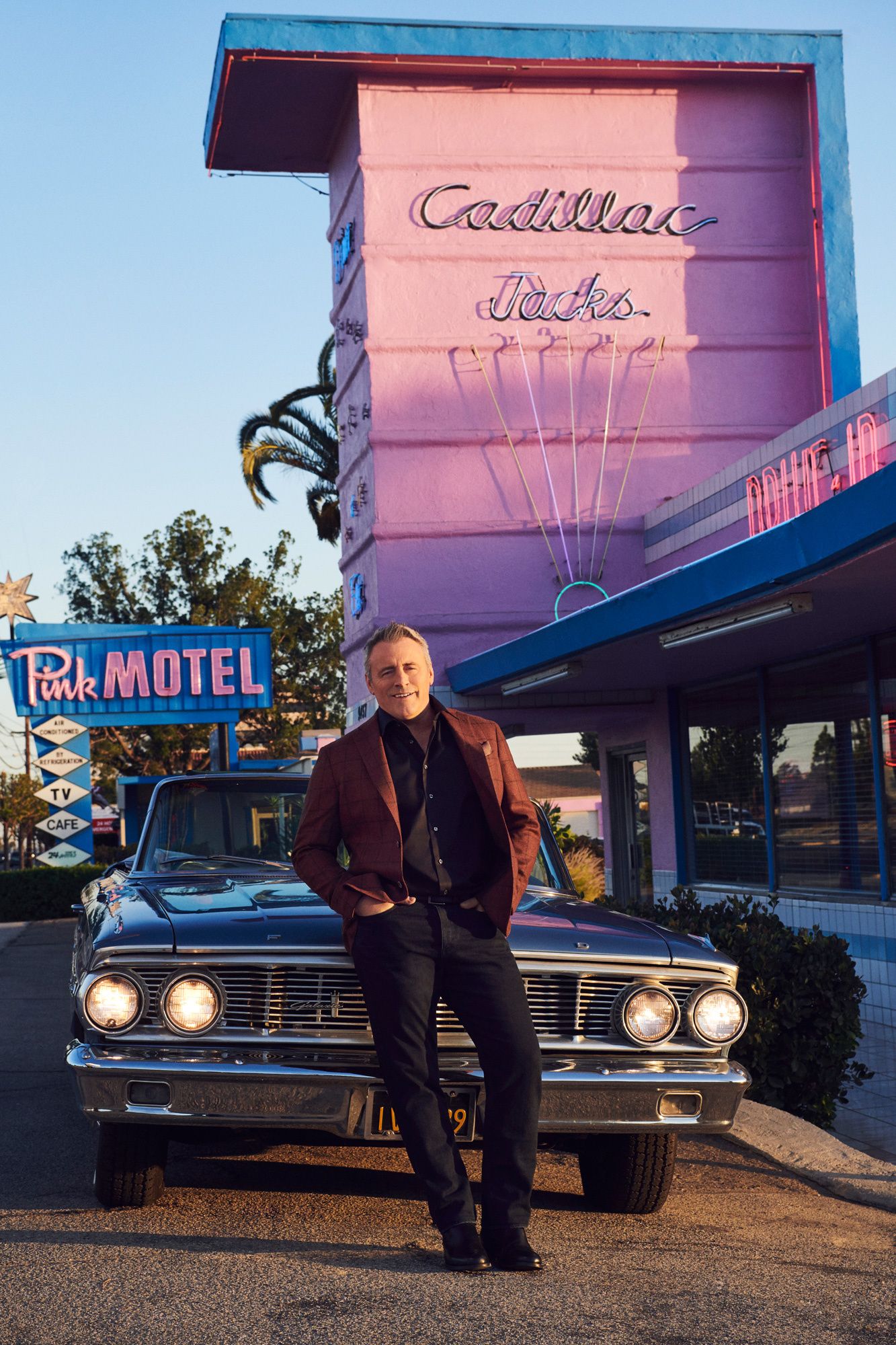 Matt LeBlanc leaning back against a vintage convertible in front of Pink Motel.