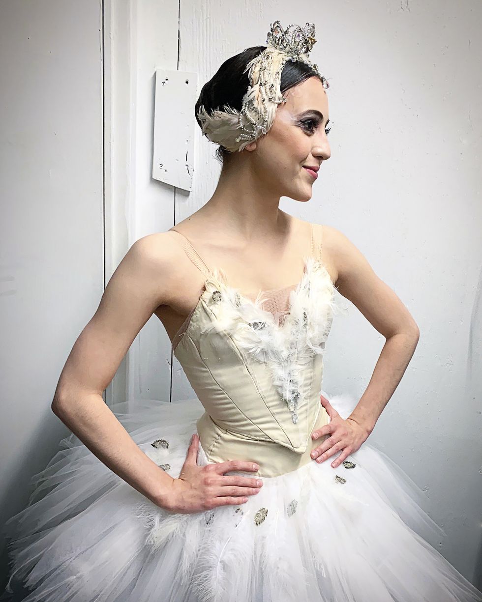 Barkman stands backstage in a white swan tutu and headpiece with her hands on her hips.