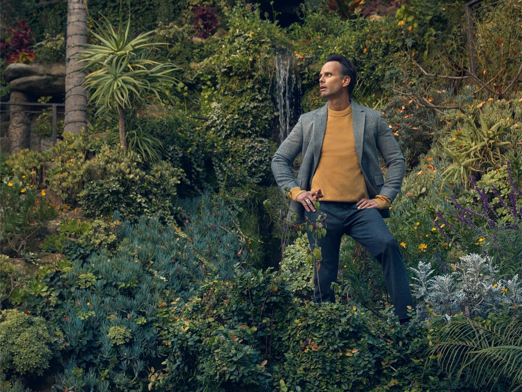 Walton Goggins standing in a beautiful landscaped garden.