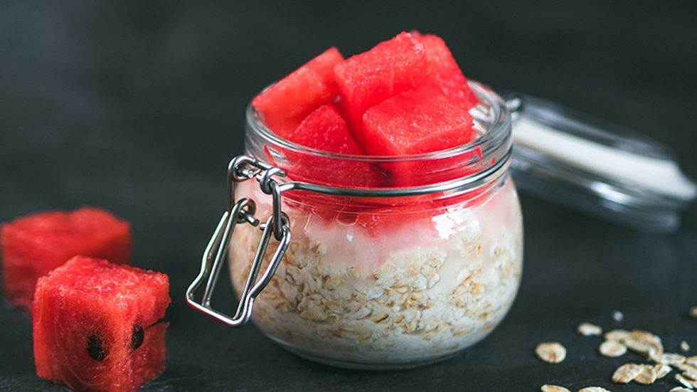 A photo of watermelon chunks on top of a glass jar of raw oatmeal.