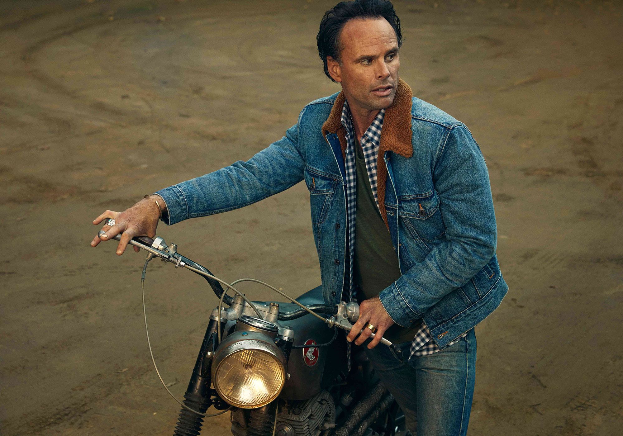 Walton Goggins wearing denim and riding a motorcycle.