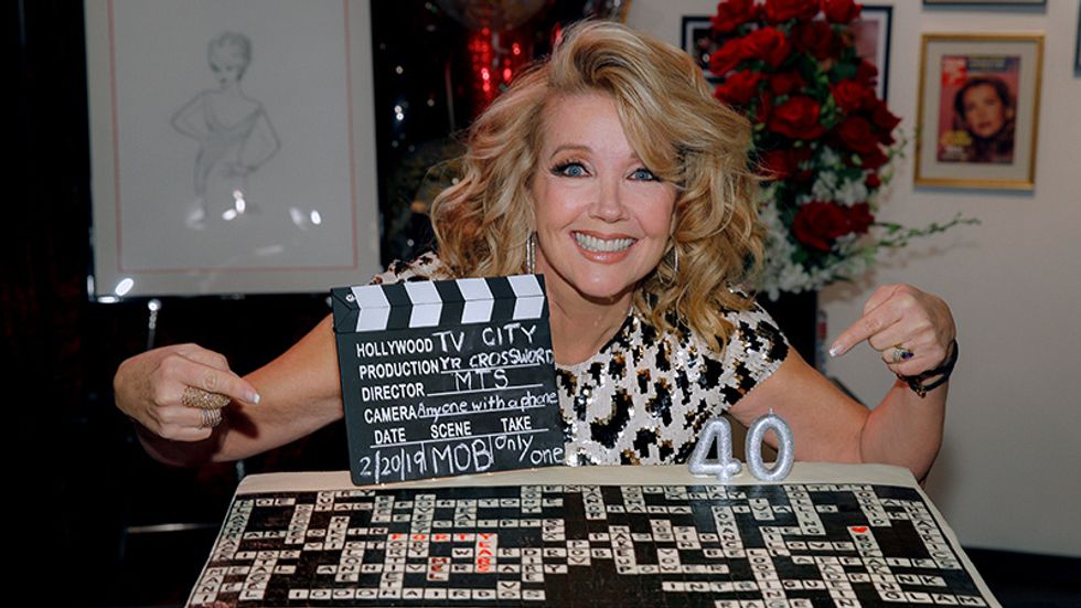 Melody Thomas Scott kneeling next to and pointing at her cake