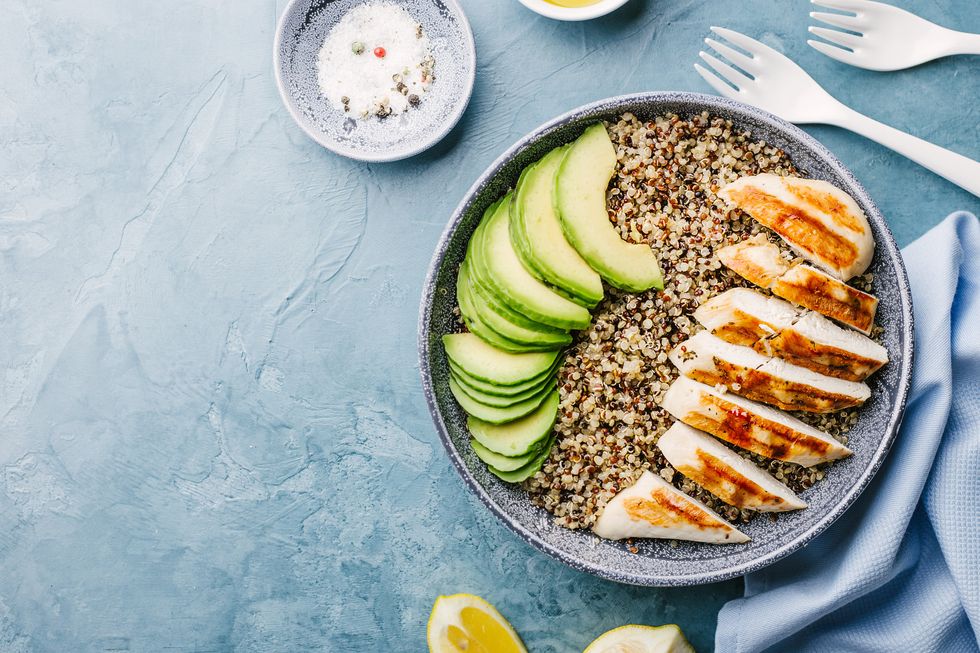 Bowl with quinoa, avocado and chicken on blue background