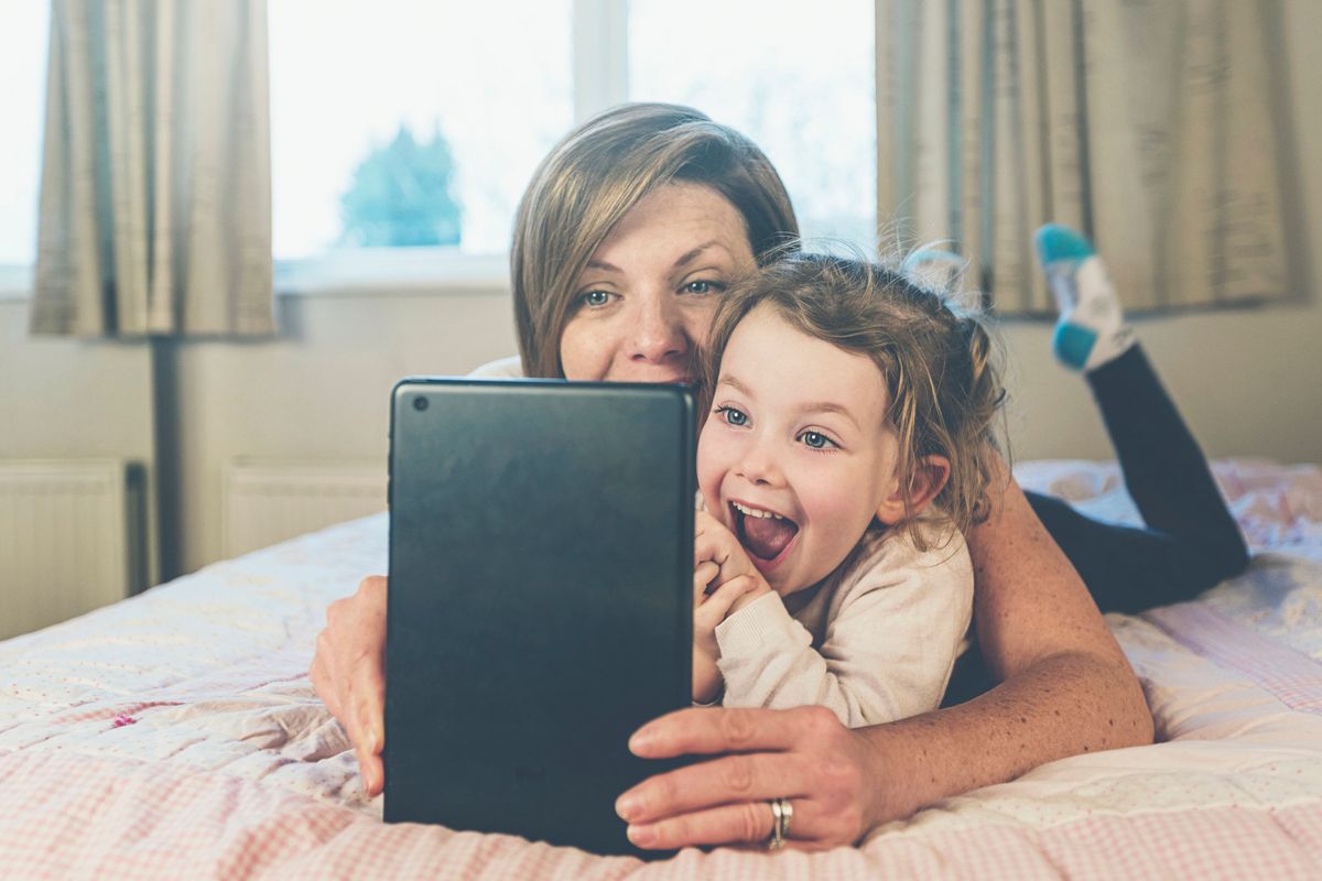 A blonde womnan and her daughter laugh at an iPad