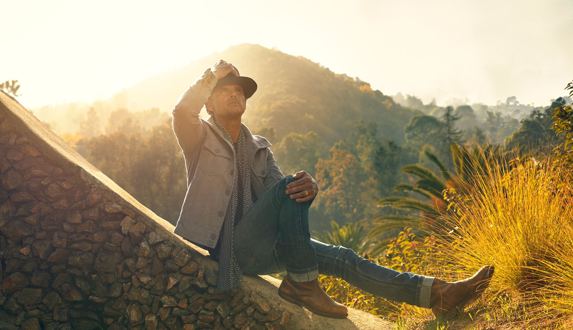 Walton Goggins sitting on a stone looking up to the sky.
