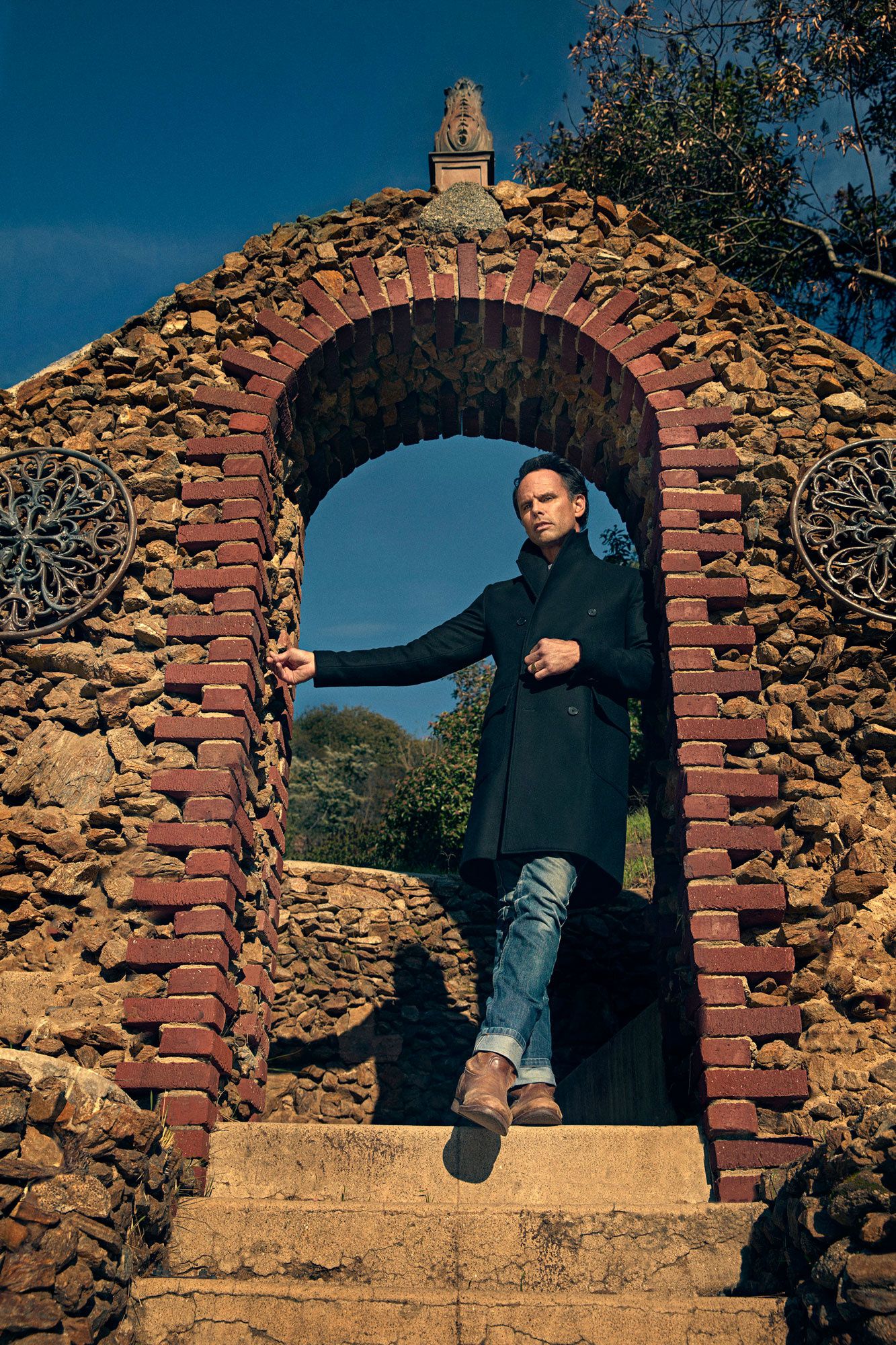 Walton Goggins standing in a stone archway.