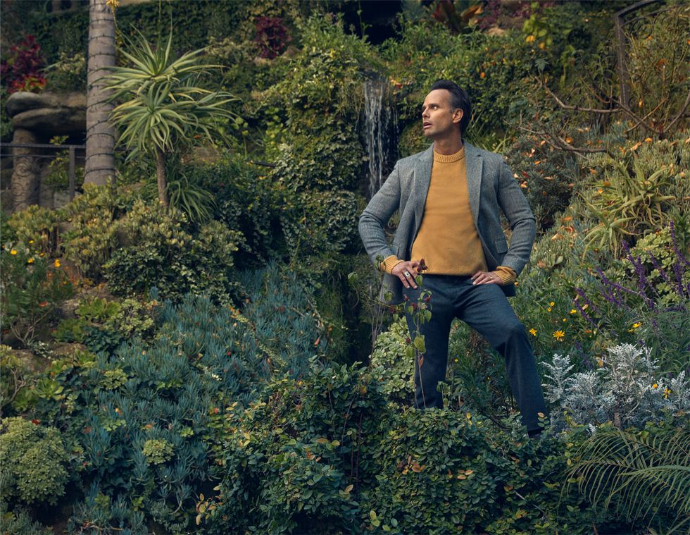 Walton Goggins surrounded by trees and foliage and a small waterfall.