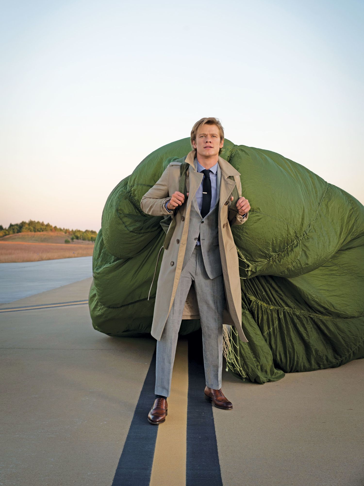 Lucas Till in a gray suit and camel jacket