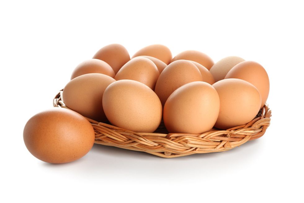 Bandeja de mimbre con huevos de gallina marrón crudo sobre fondo blanco.