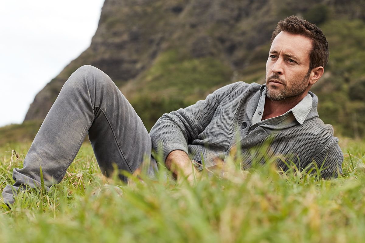 Alex O\u2019Loughlin laying in grass wearing gray sweater