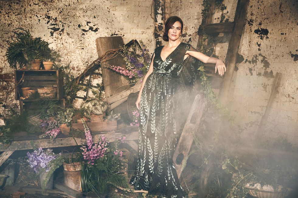 Maggie Siff in a floral dress among floral arrangements.