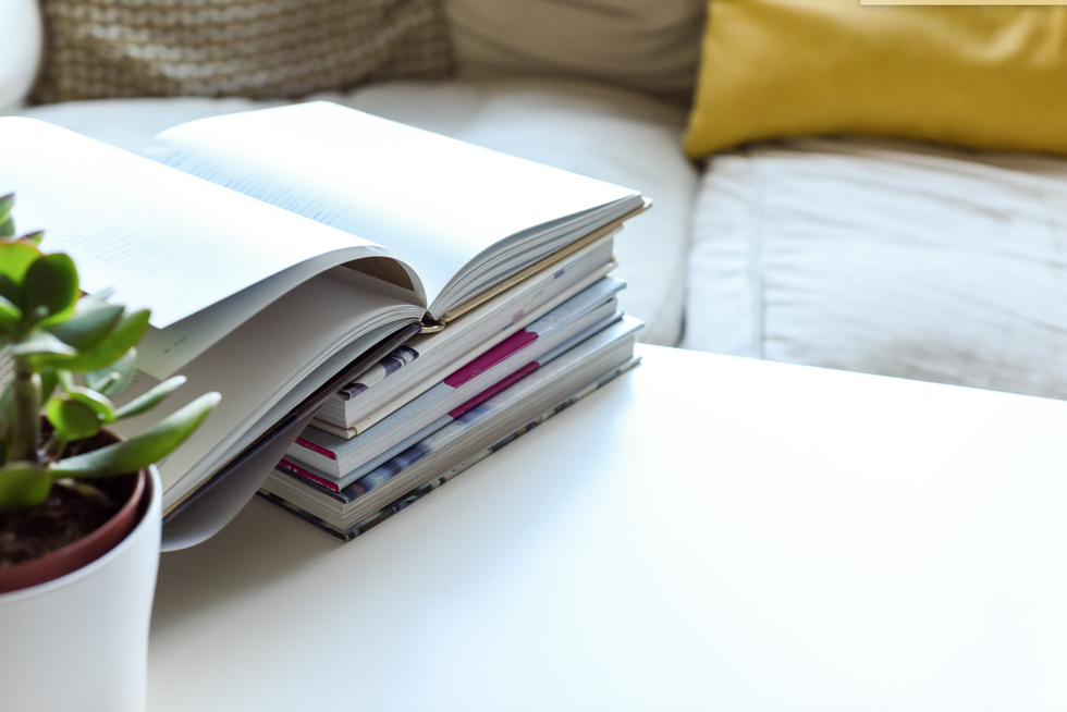 Small stack of books on a white table next to a white couch with yellow pillows on it.