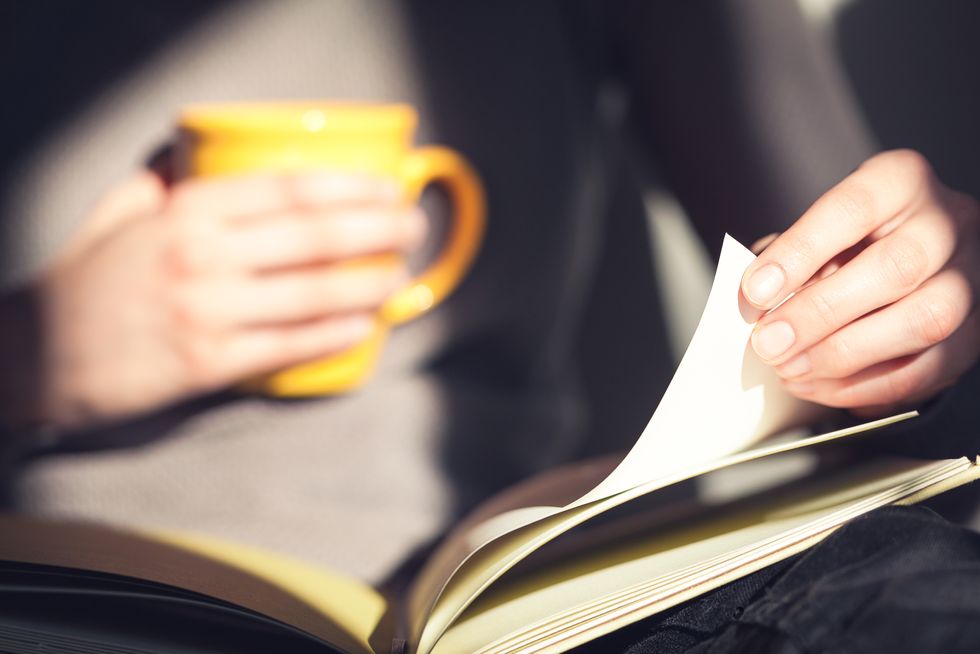 Close up of a woman's hands holding an open book and a yellow mug.