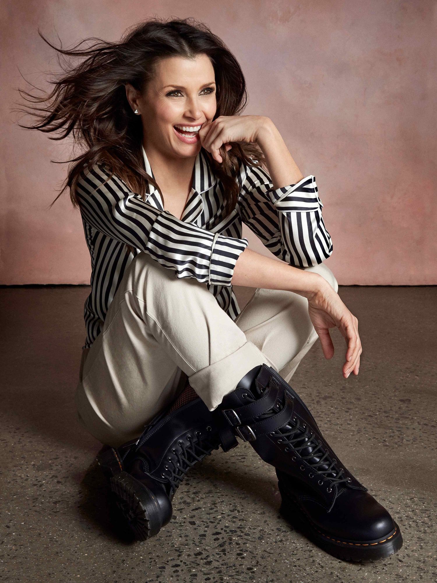 Bridget Moynahan sitting wearing striped shirt and black leather boots