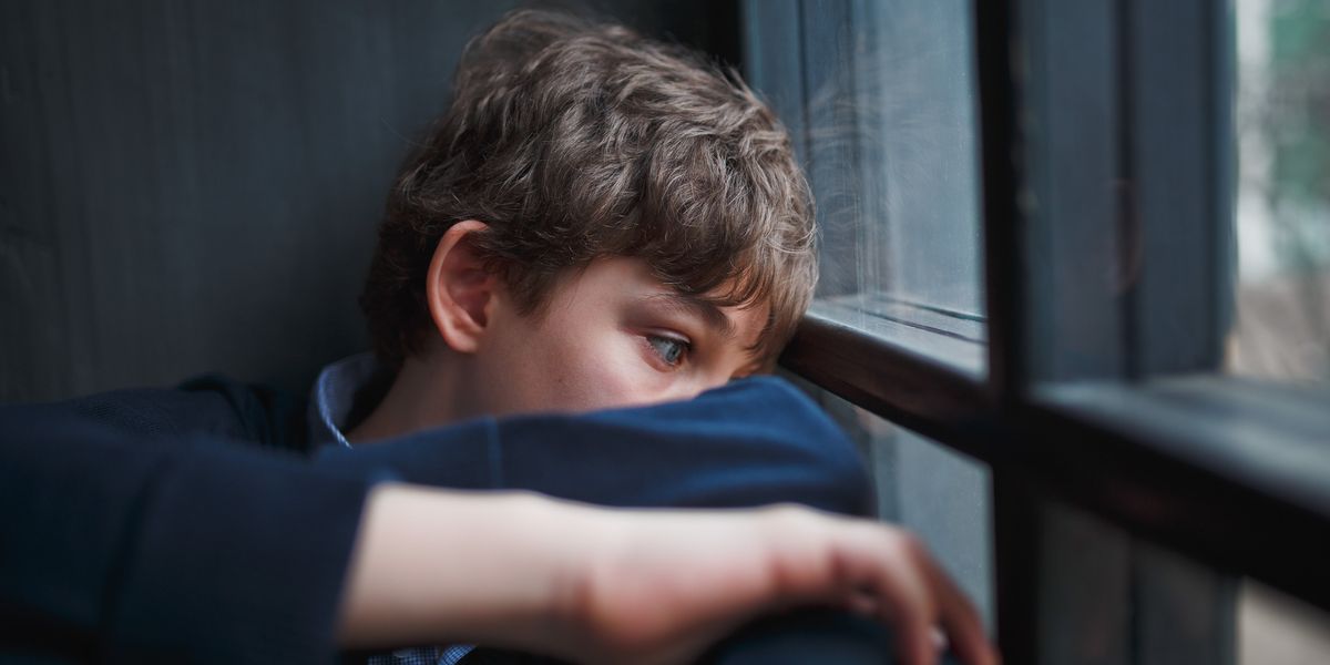 Distracted or sad young boy looking out window