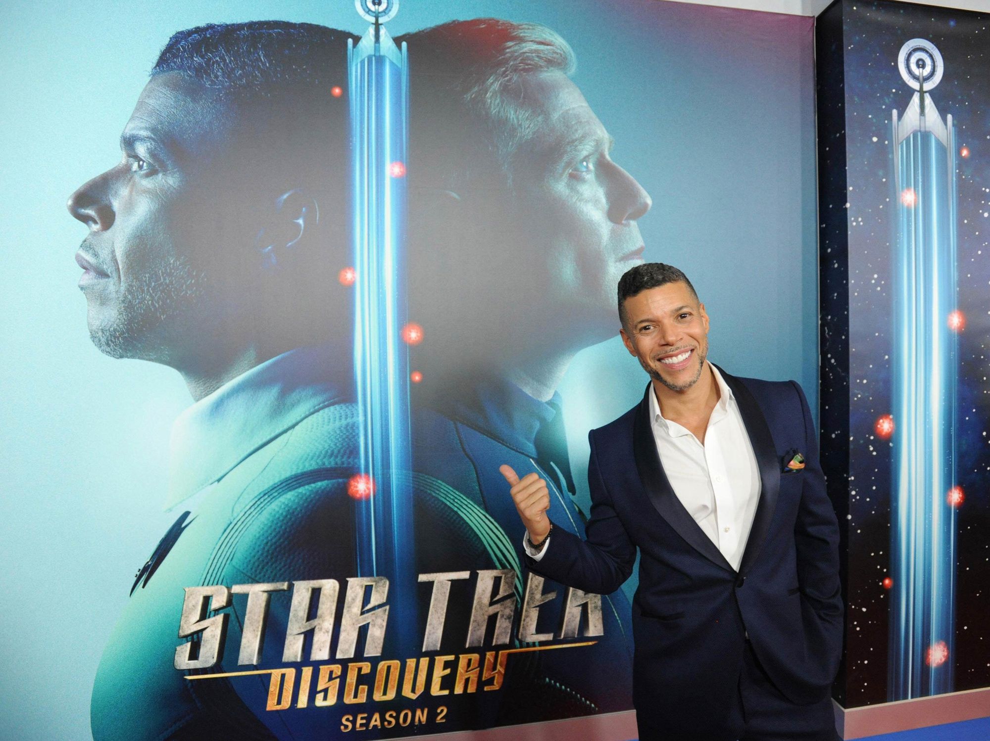 Wilson Cruz posing in front of a Star Trek: Discovery poster.