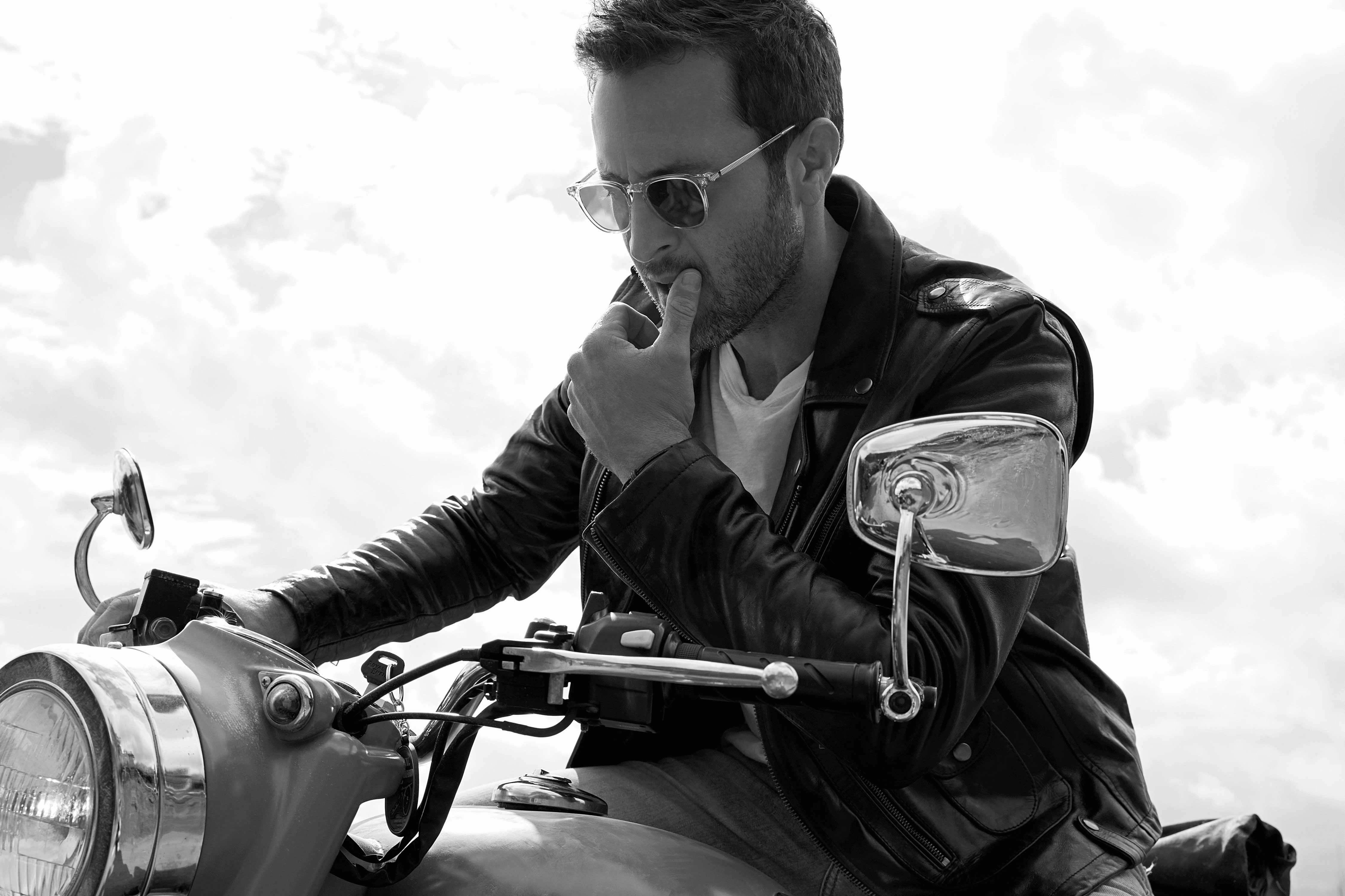 Black and white photo of Alex O'Loughlin riding a vintage motorcycle.