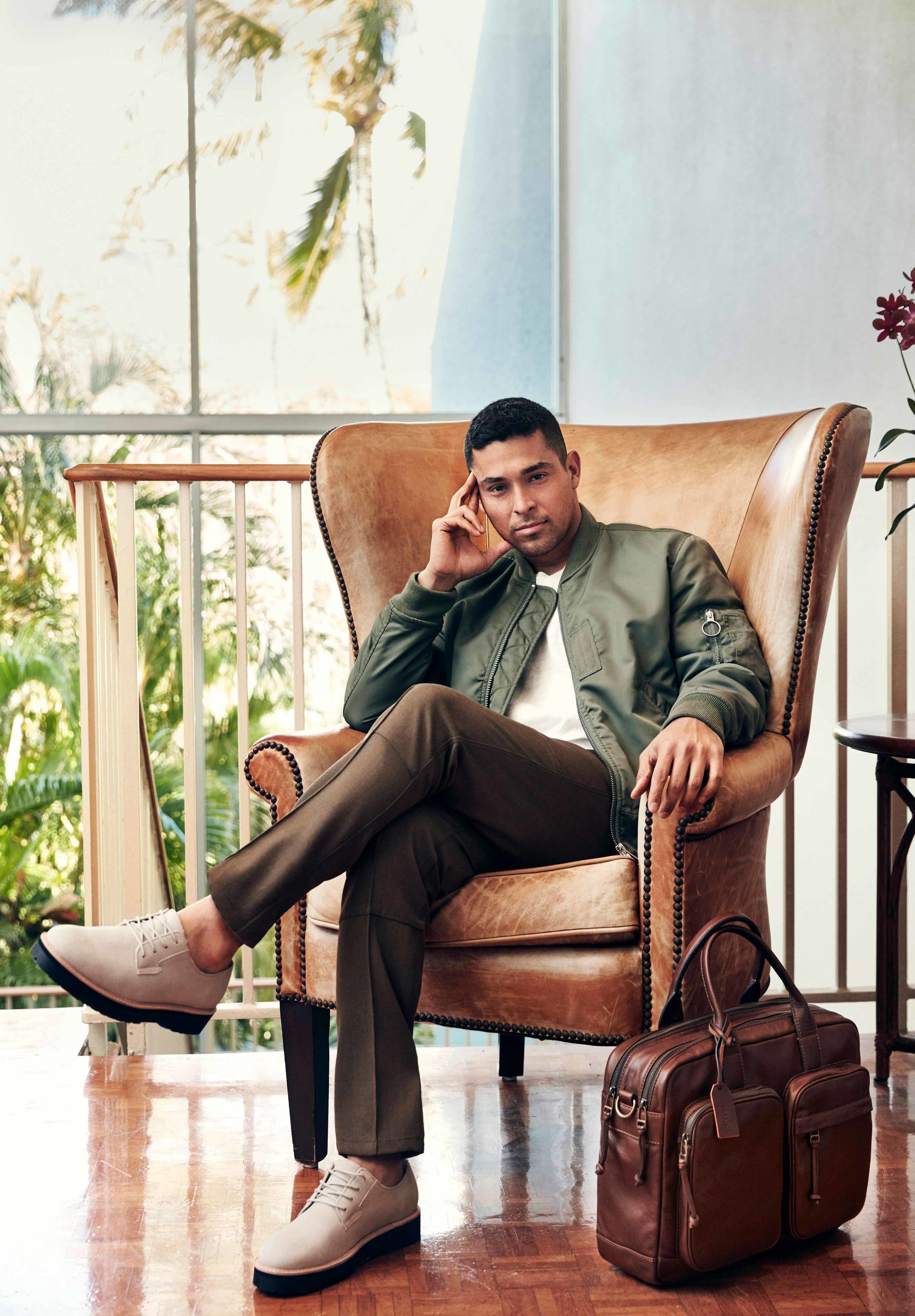 Wilmer Valderrama sitting indoors in a light brown leather chair leaning his temple on his hand