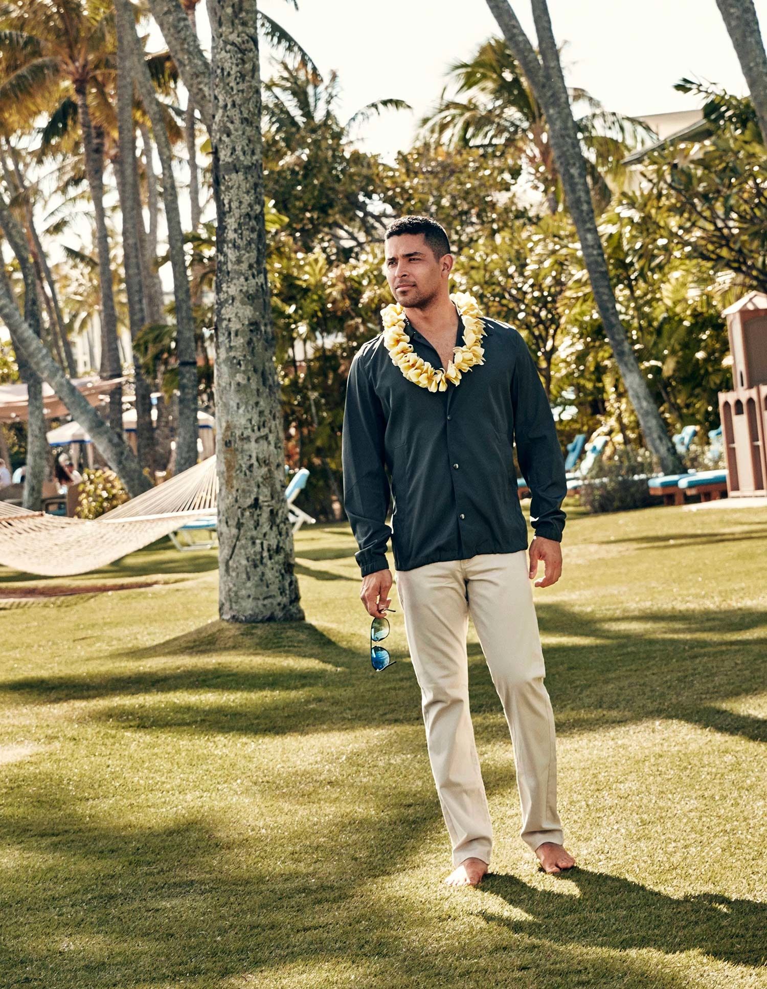 Wilmer Valderrama barefoot on the grass wearing a yellow lei and a green button down shirt