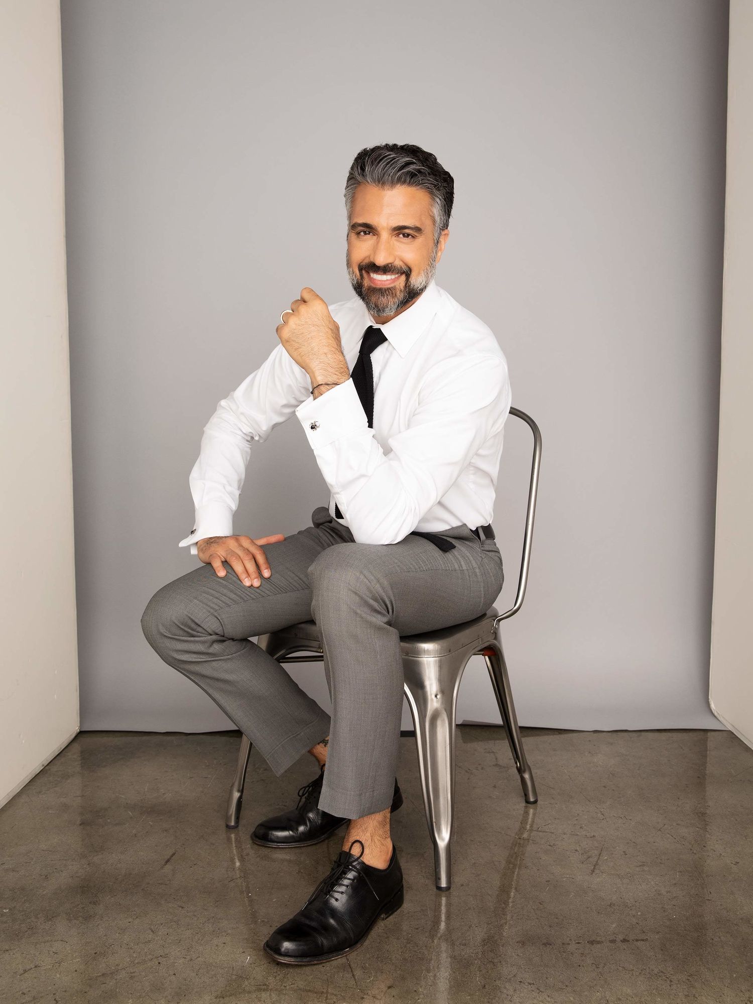 Actor Jaime Camil sitting on a sitting chair and smiling.