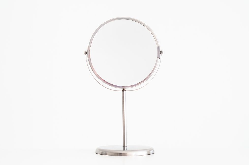 Single magnifying beauty mirror on stand isolated against pure white front view