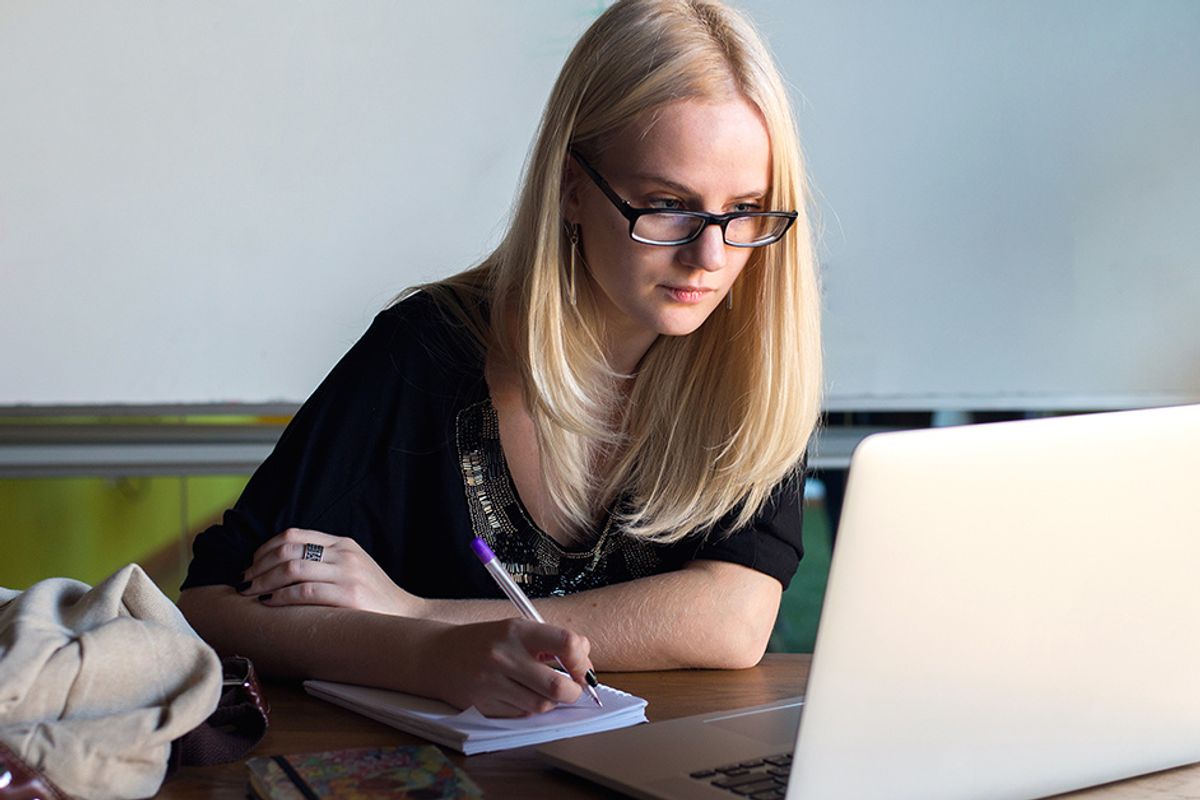 blonde woman writing near a laptop