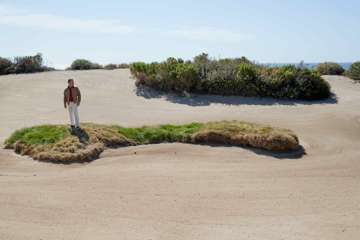 Chris ODonnell standing on a grassy hill surrounded by sand on a gold course