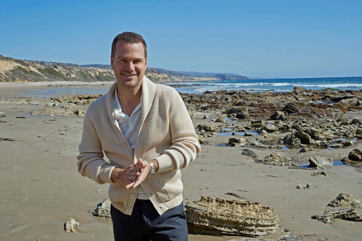 Chris O'Donnell wearing a cream cardigan and walking on the beach