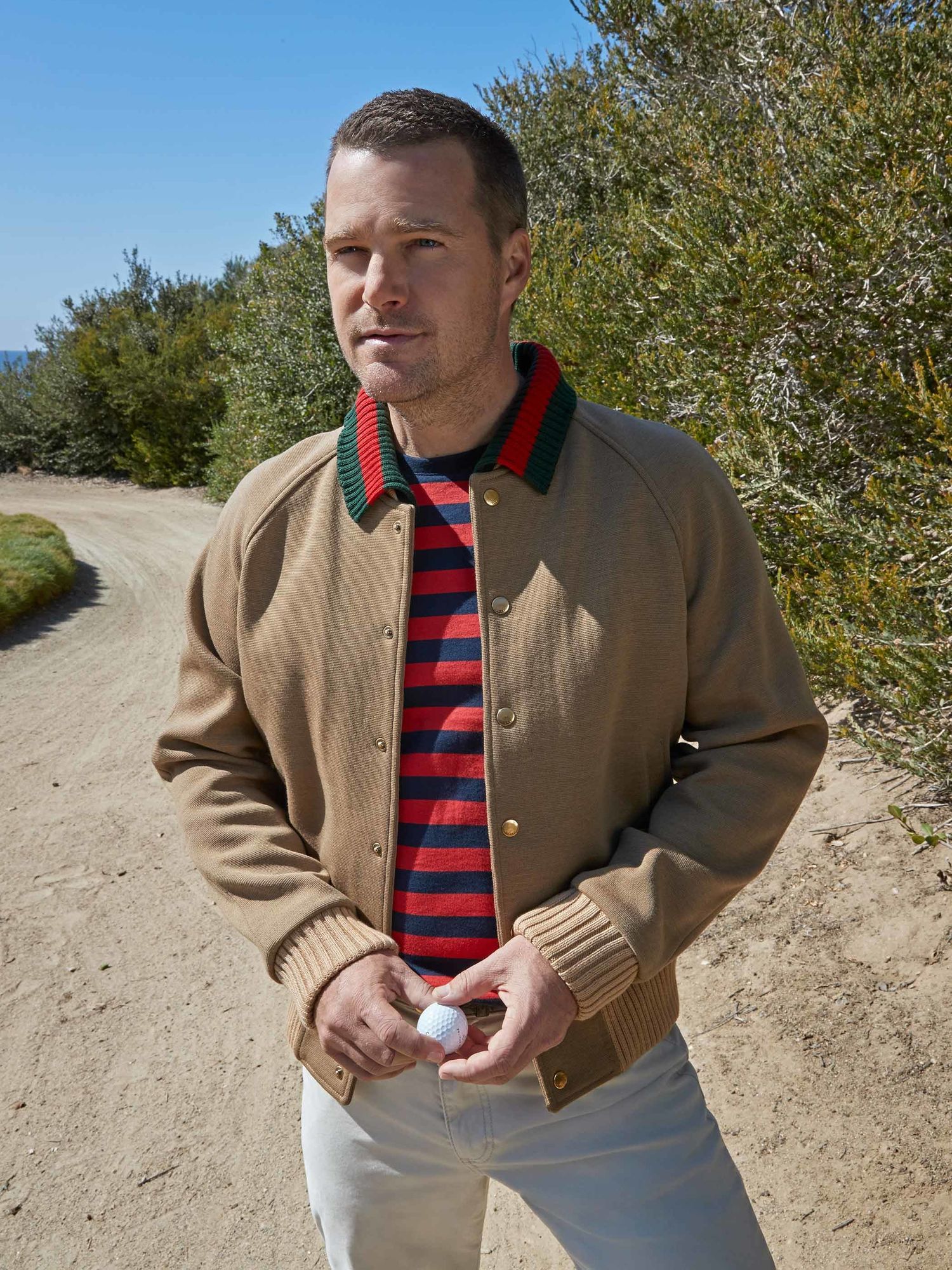 Chris ODonnell in a red and blue striped shirt and camel jacket staring off into the distance