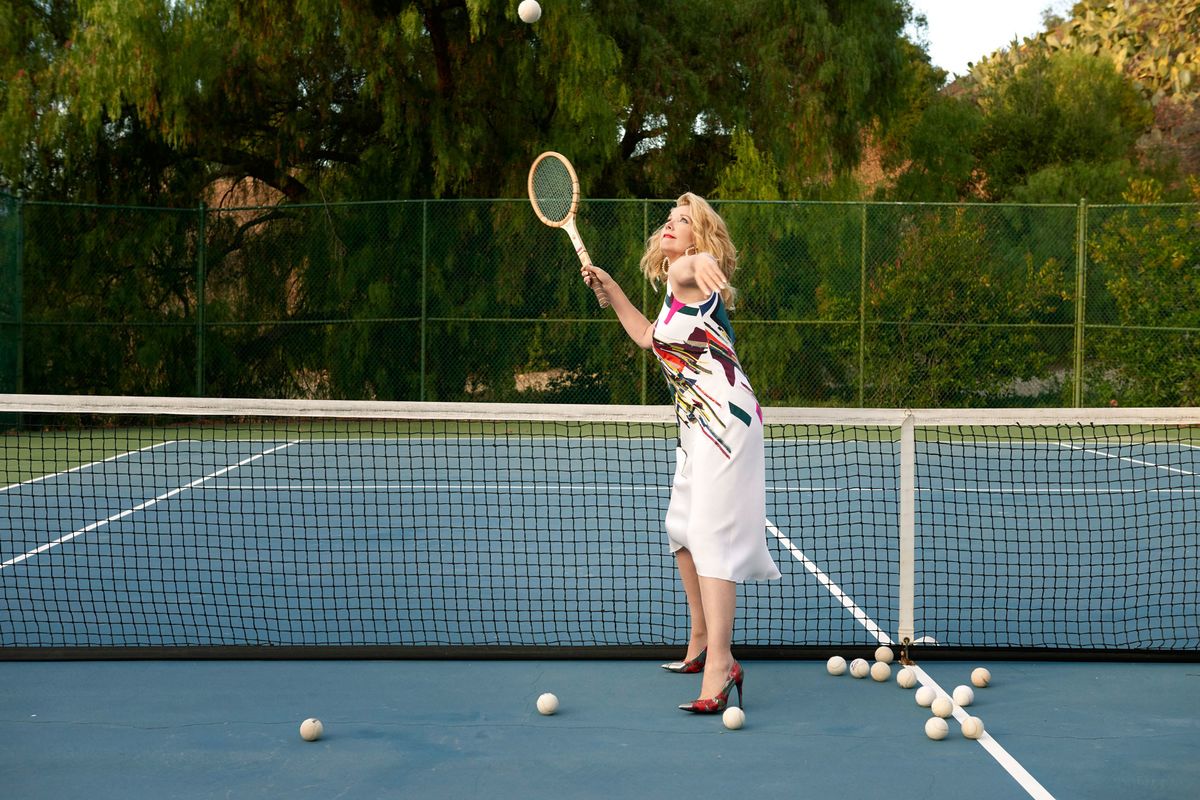 Melody Thomas Scott serving on a tennis court in high heels