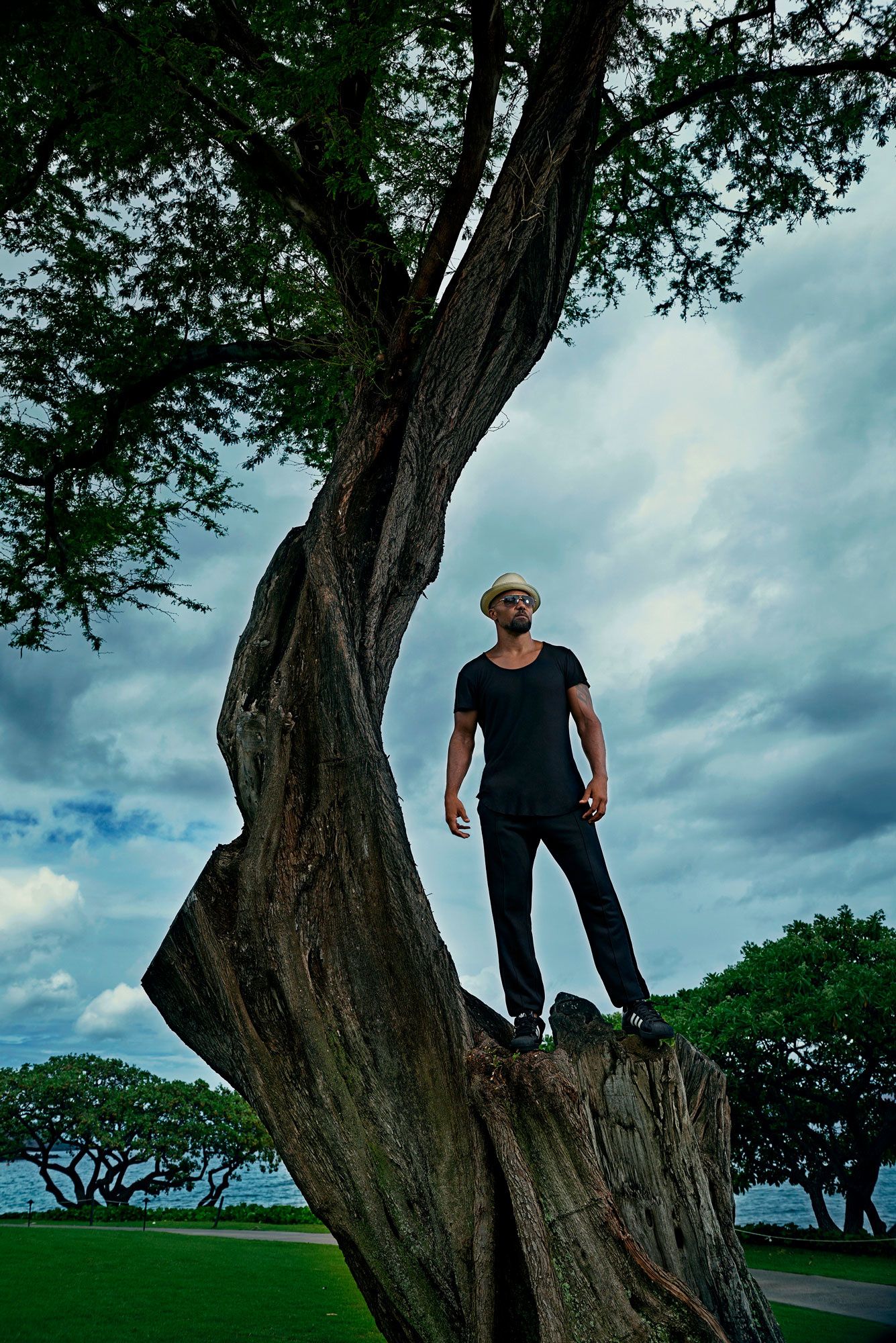 Shemar Moore standing on a broken tree trunk in a black top and pants
