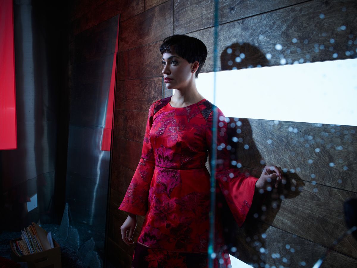 Actress Cush Jumbo leaning against a wall in red dress.