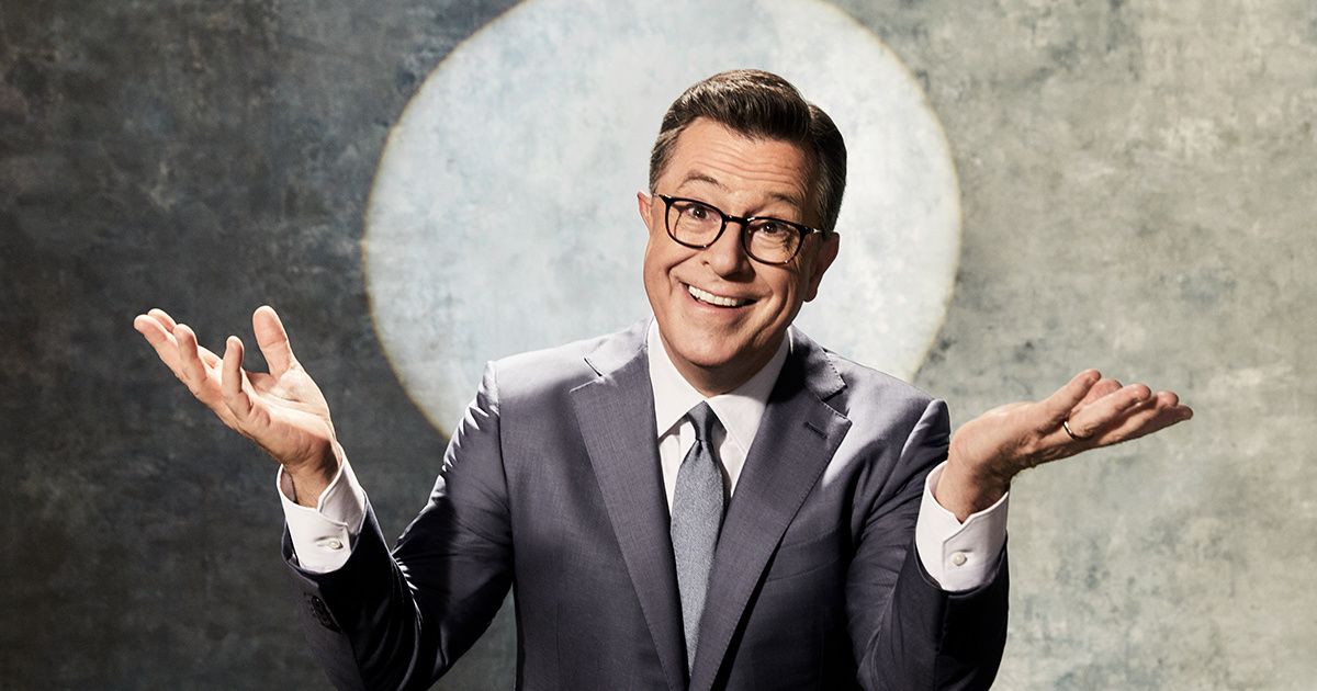 Stephen Colbert in a suit with a spotlight behind him.