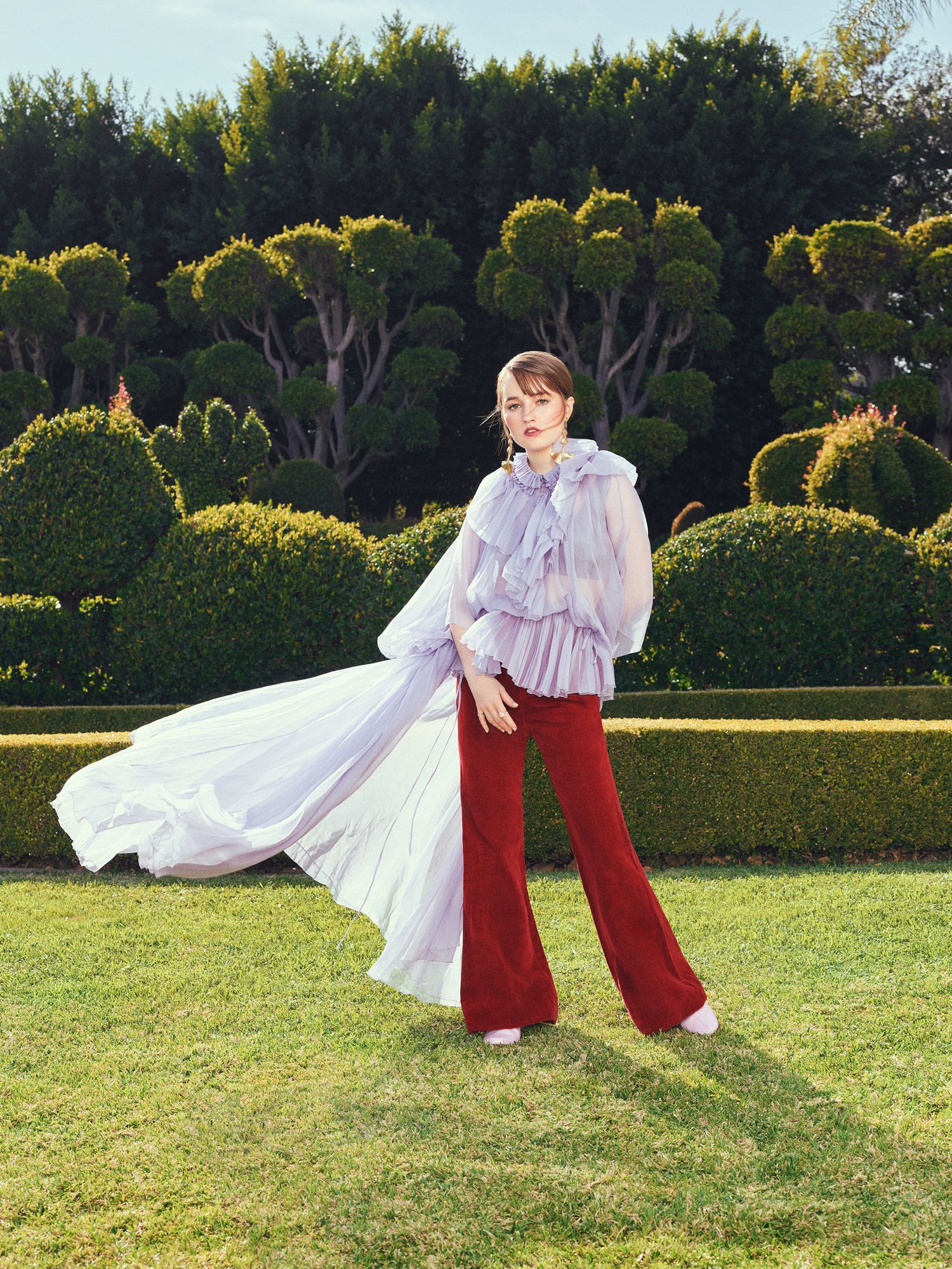 Katilyn Dever in a modern garden wearing red pants and a long flowing top.