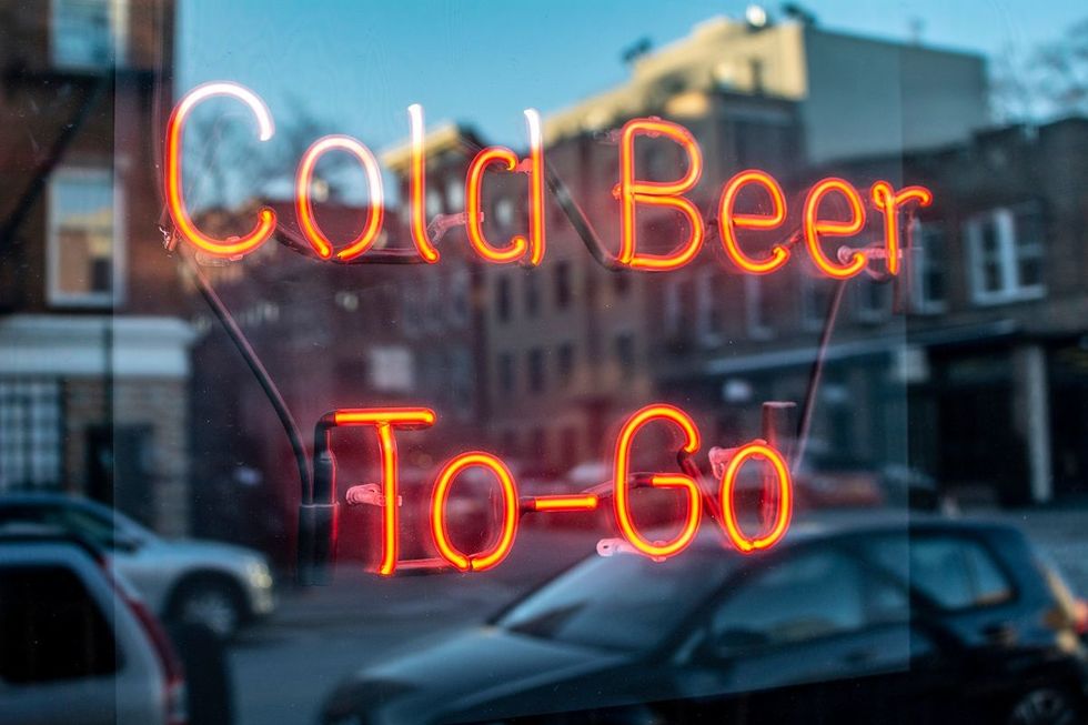 A red, neon sign on a restaurant window promises "Cold Beer To-Go."