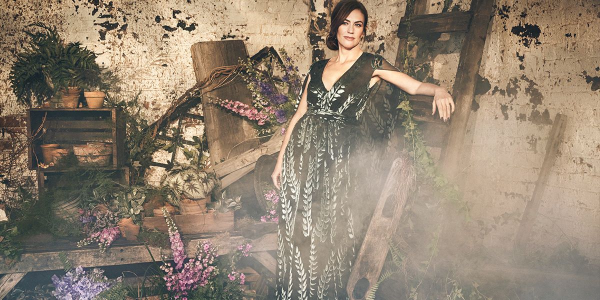 Maggie Siff in a floral dress among floral arrangements.