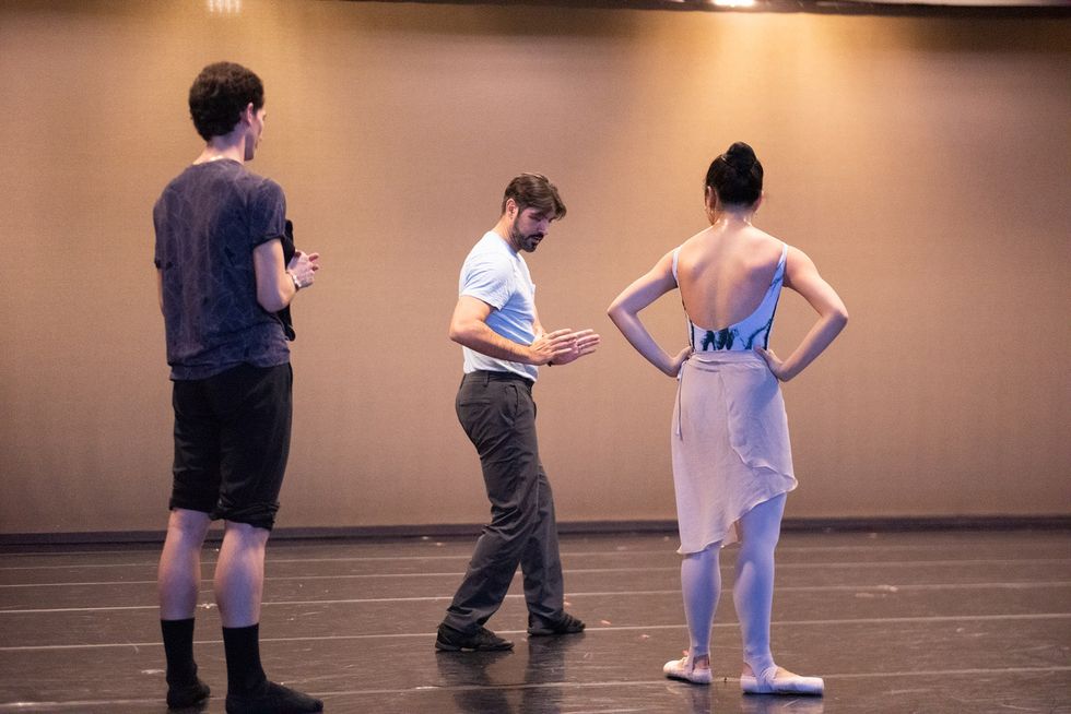 Martin stands onstage with two dancers, using his hands to demonstrate in rehearsal.