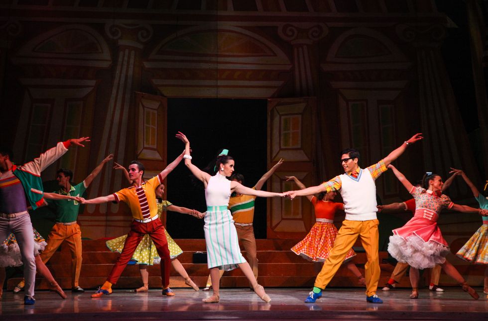 Dancers dressed in colorful 1950s style costumes onstage doing a social dance step