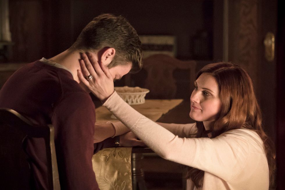 Barry Allen in a chair and having his face held by his kneeling mother Nora Allen played by actress Michelle Harrison
