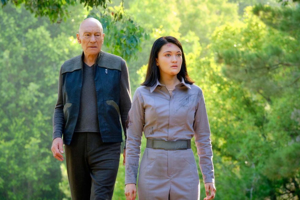 Actress Isa Briones walks with Patrick Stewart on a forested scene.