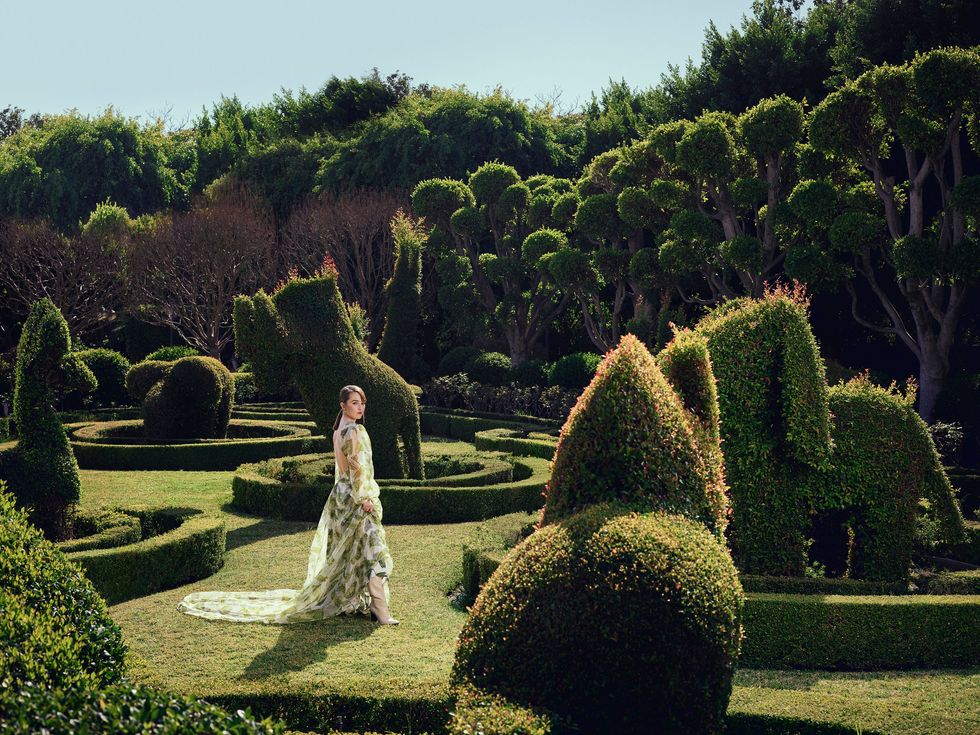 Actress Kaitlyn Dever wears a flowing butterfly print dress in a groomed topiary garden.